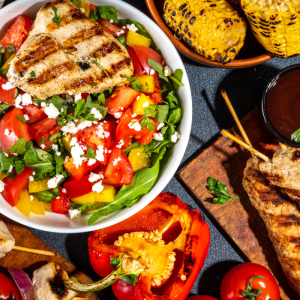 Assorted picnic and grilled foods including burgers, kebabs, fresh salad, vegetables, and barbecue dishes displayed on a table for a Foodie Club event.