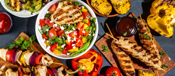 Assorted picnic and grilled foods including burgers, kebabs, fresh salad, vegetables, and barbecue dishes displayed on a table for a Foodie Club event.