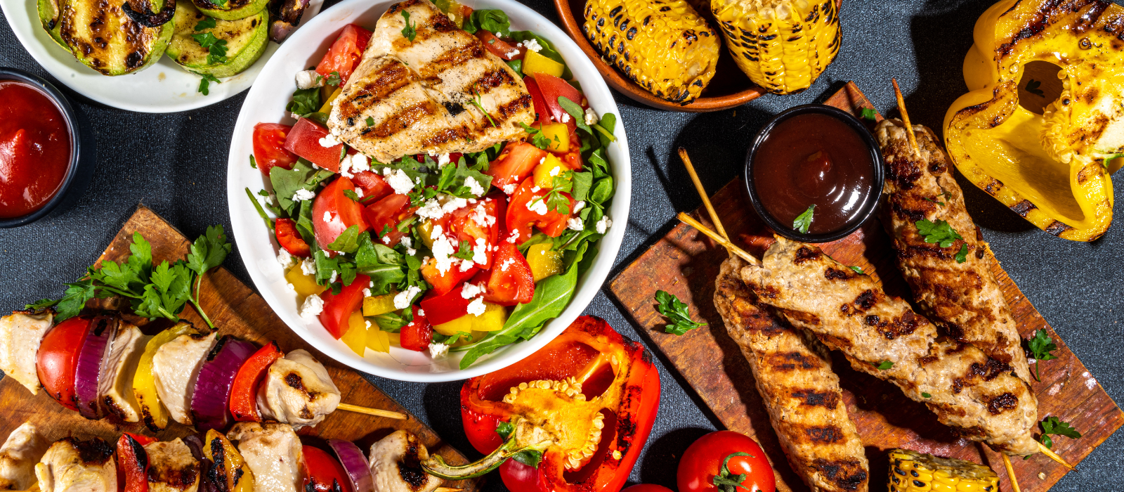 Assorted picnic and grilled foods including burgers, kebabs, fresh salad, vegetables, and barbecue dishes displayed on a table for a Foodie Club event.