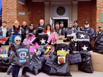 Worth Township staff, volunteers, and motorcycle club members pose outside the Township building with donated toys, winter coats, and bags collected during the annual holiday toy drive.